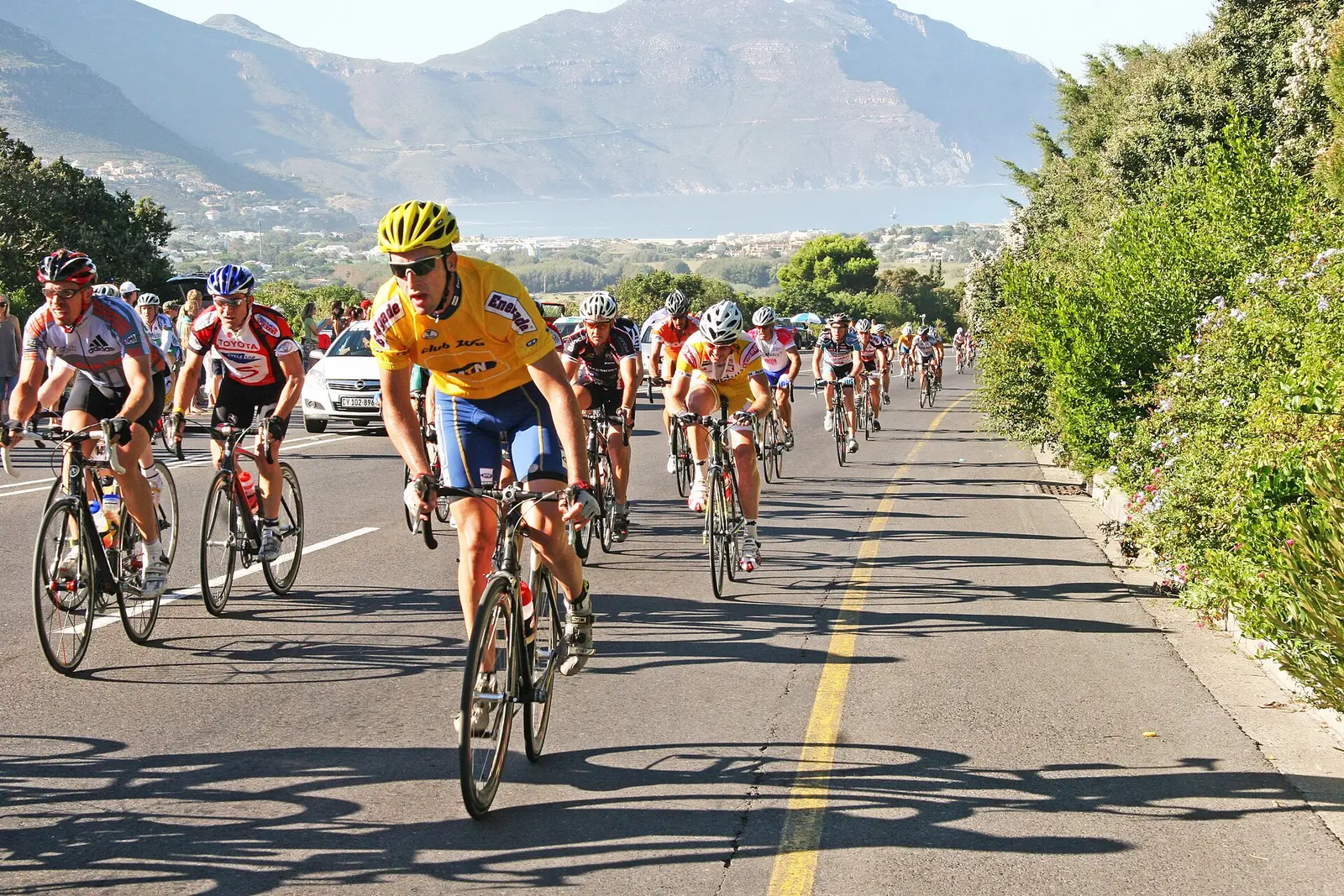 Cyclists riding a coastal road in the Cape Argus Cycle Tour with mountains behind