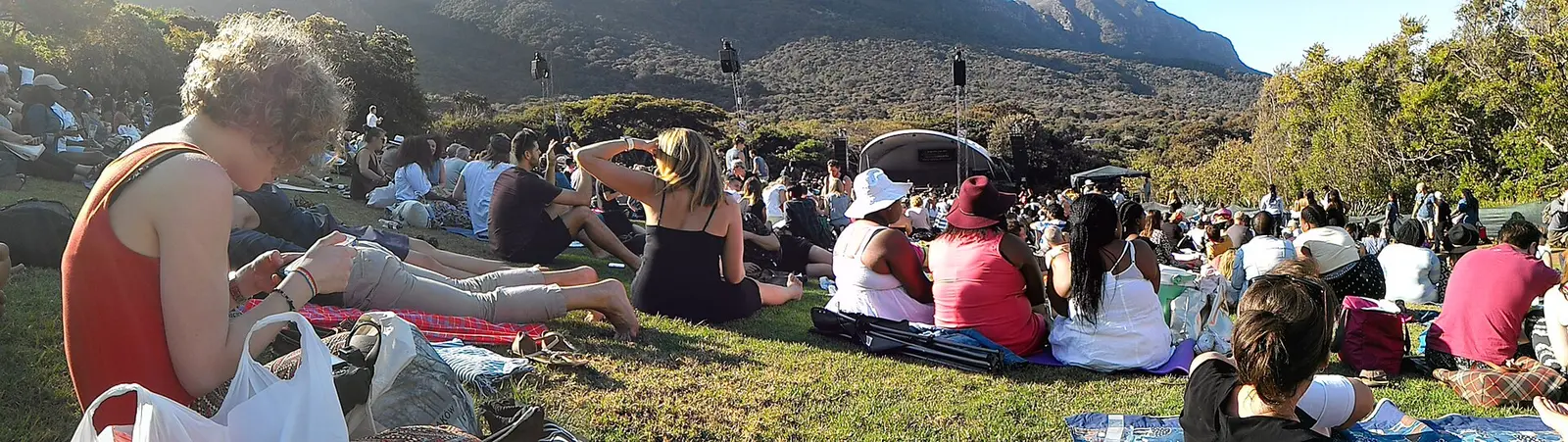 Audience seated on the lawn at a Kirstenbosch concert with the mountain behind the stage